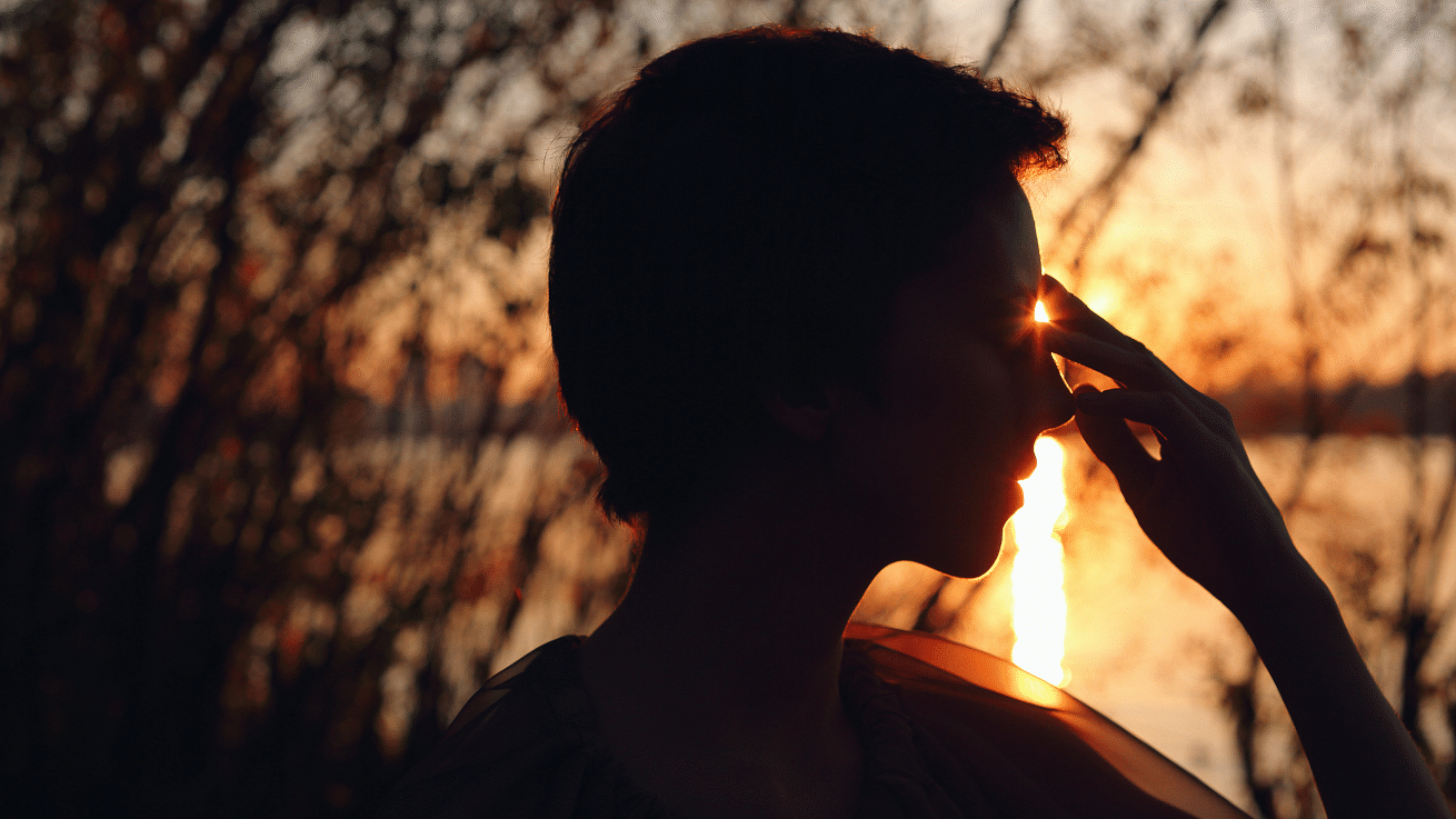 Silhouette of a person touching their forehead against a sunset backdrop.