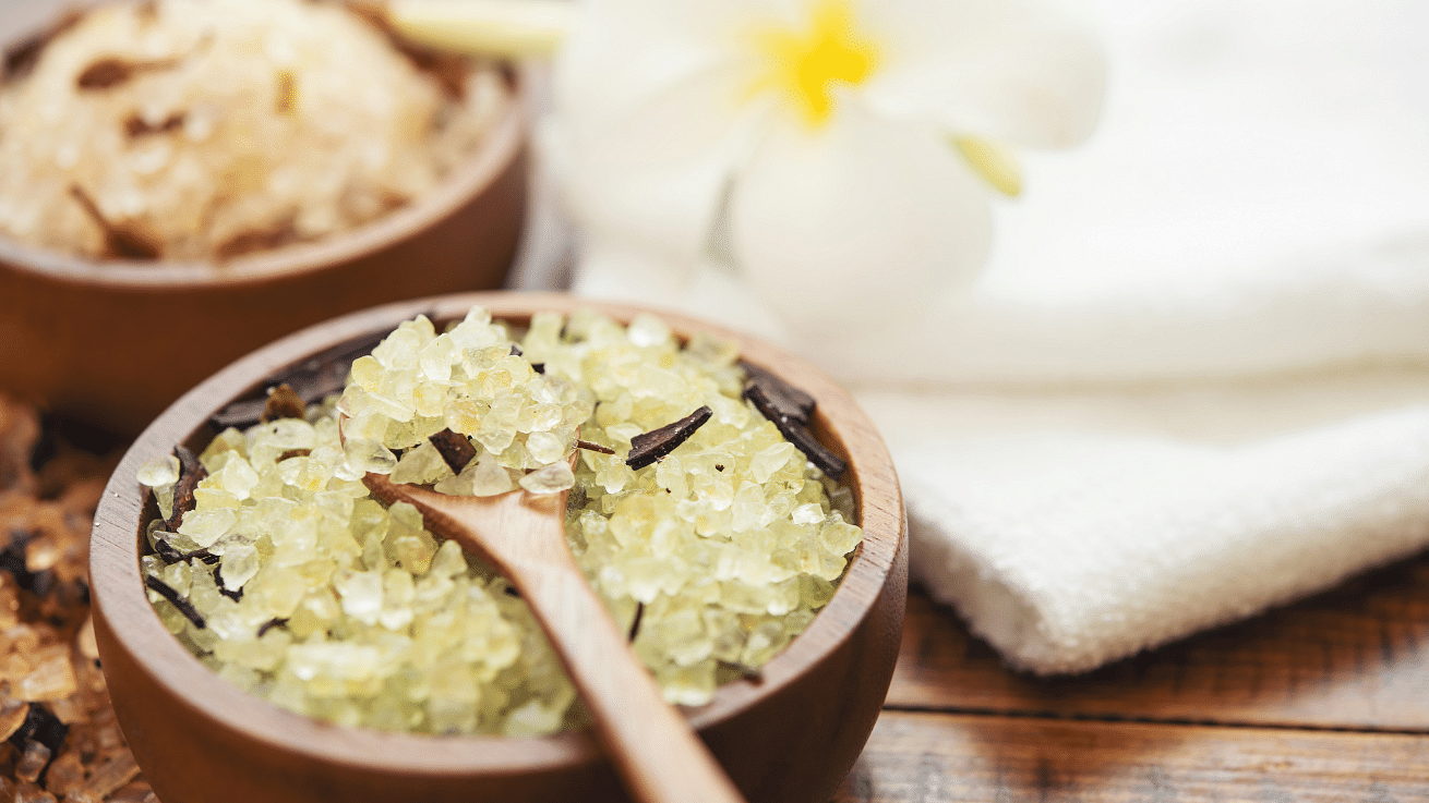 Himalayan salt scrub in a wooden bowl and spoon next to a white towel. 