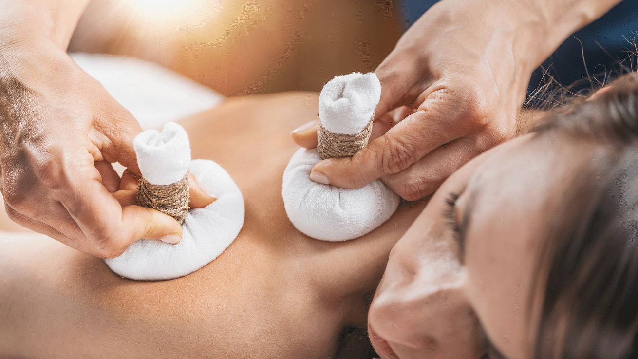 A person receiving a back massage with herbal compresses.