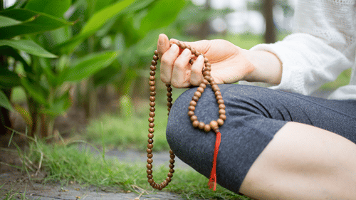 Close-up of a hand holding prayer beads during a meditation practice outdoors.