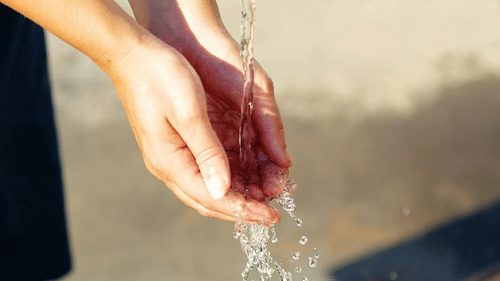 Cupped hands catching clear, sparkling water from a tap, symbolizing cleanliness or refreshment.