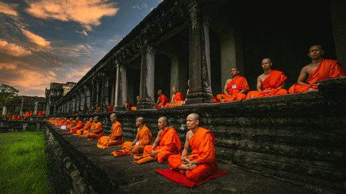 Monks in orange robes meditating in a historical temple at sunset.