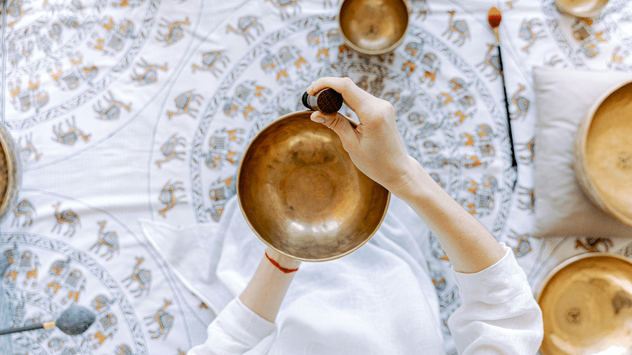 An overhead view of a person's hands holding a Tibetan singing bowl with a patterned fabric underneath.