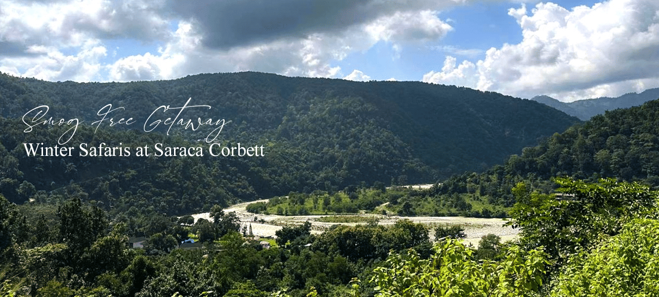 Scenic landscape of a resort nestled among rolling green hills under a clear blue sky, highlighting a tranquil nature retreat, with Smog Free Break Saraca Corbett written on the image.