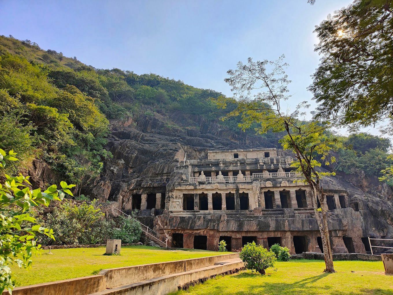 An ancient stone temple ruin is nestled within a verdant, hilly landscape under a bright sky.
