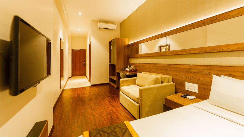 The Executive Room at Residences at CSE showcasing a double bed. a flat screen television, a multi-seating sofa, and wooden flooring.