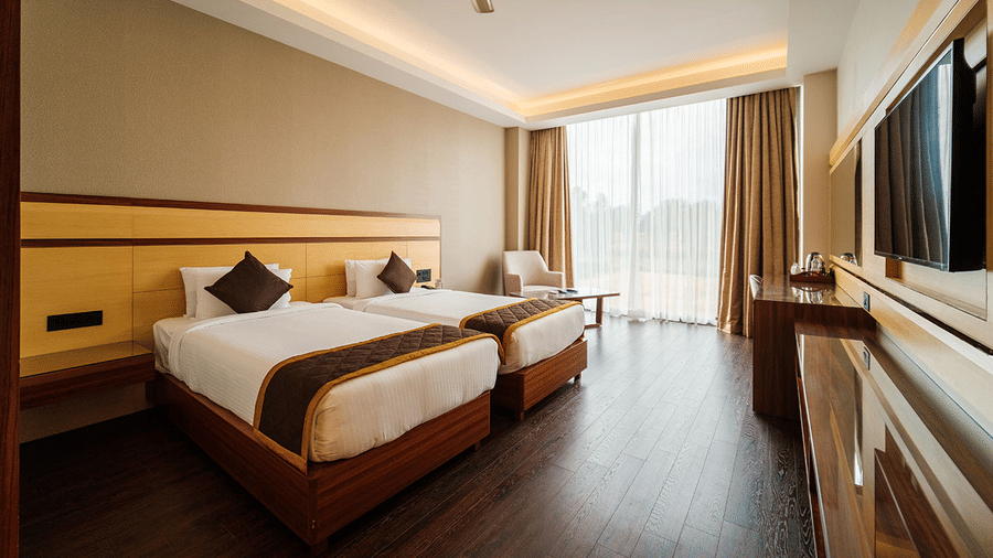 A spacious hotel room with twin beds, a wardrobe, a television, and a view of the outdoors. at The Residences at CSE, Banglore