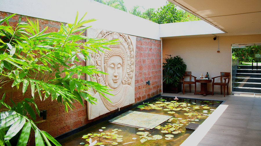Outdoor lounge area with a Buddha wall sculpture and pond with floating leaves.