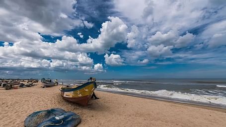 A fishing boat rests on a sandy beach as waves meet the shore under a dramatic, cloud-filled sky
