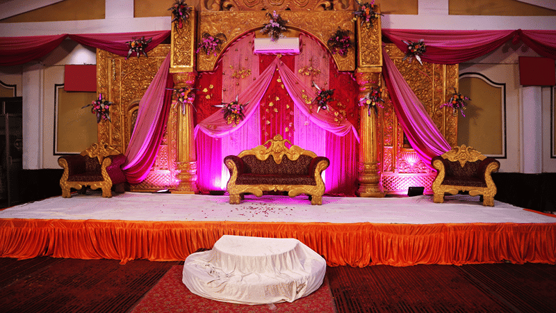 Wedding stage setup at Lime Tree Hotels & Service Apartment Private Limited featuring pink drapes and floral decorations.