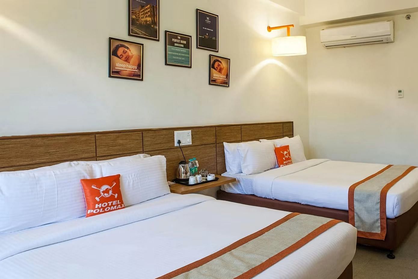 full view image of the max family room featuring two plush double beds along with a split air-conditioner and a bedside table between the two beds - Max Hotel Jabalpur