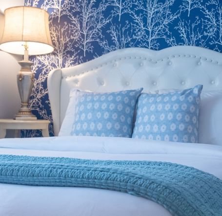 A bedroom with white tufted headboard, navy tree wallpaper, blue pillows and teal throw blanket at Hartstone Inn.