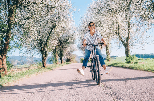 A woman riding a bicycle in an empty road with trees around on a sunny day