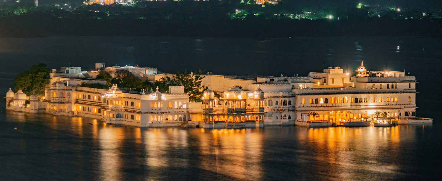 An aerial view of a palace in middle of a water body illuminated by bright yellow lights