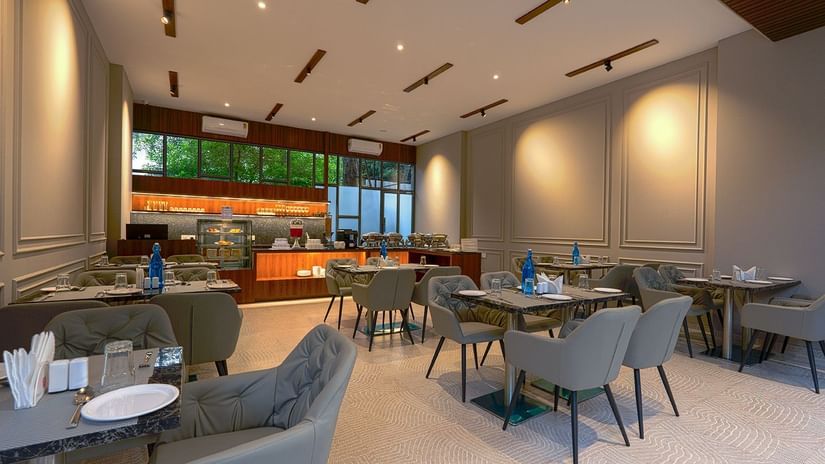 Restaurant at Magnus Nexstar Suites, Kalyani Nagar featuring table and chairs across the dining space. There is also a shelf where foot and utensils are kept.