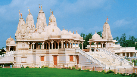 A large, white temple with many domes on a green lawn.