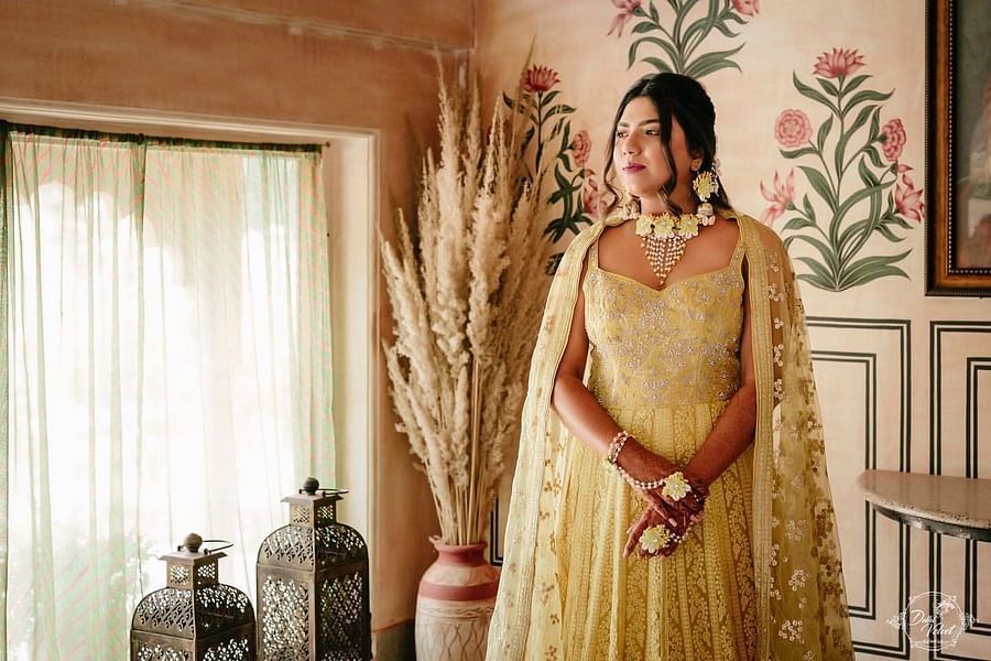 A bride in a embellished outfit poses elegantly in a floral-themed room, adorned with pearl and floral jewelry.- Umaid Palace - A Lakeside Heritage Palace Resort