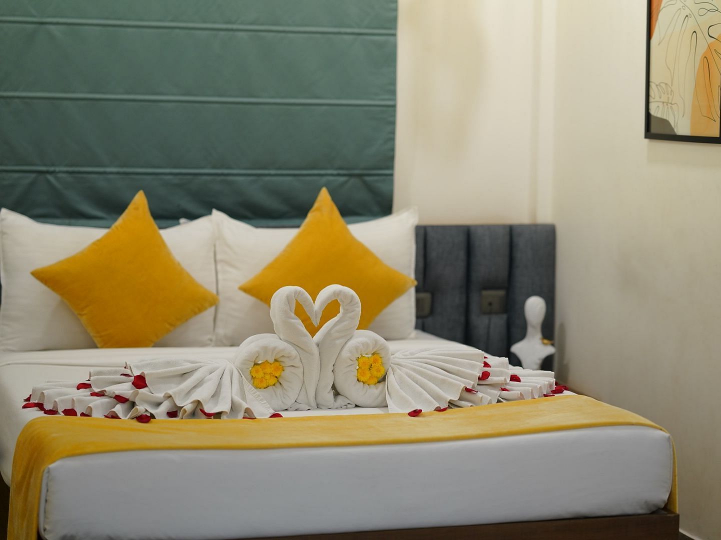 A room with a neatly made double bed adorned with yellow and towels shaped into swans, scattered with rose petals for a welcoming touch at Hotel Kyzen Smartstays – Smart, Reliable, Kyzen