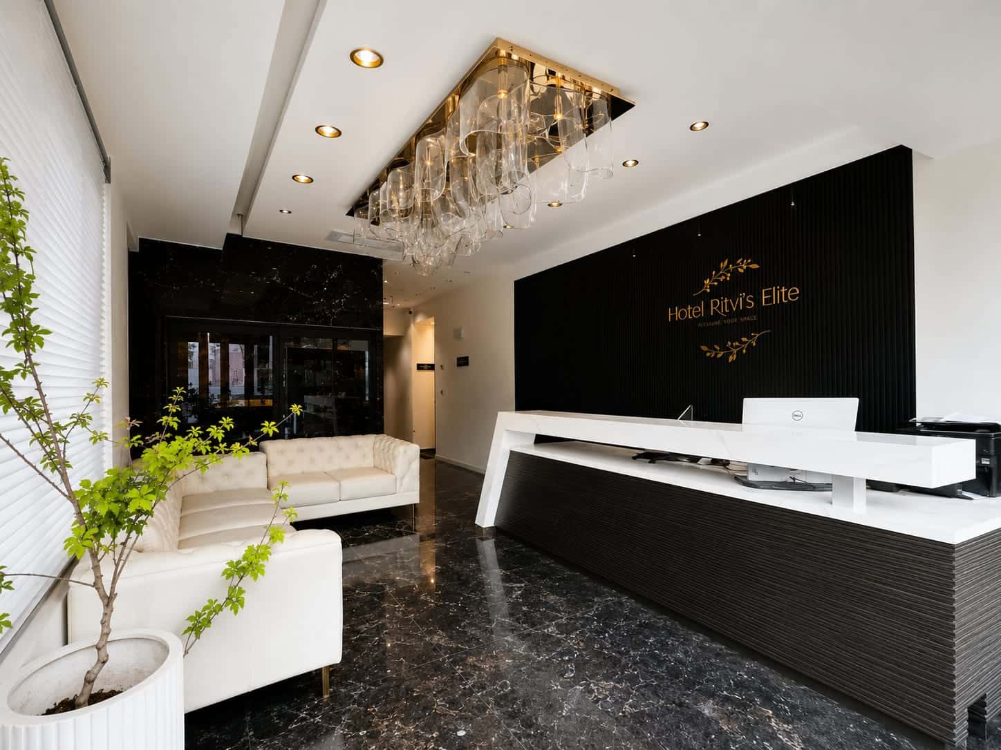 Reception at Hotel Ritvi's Elite, a white marble-topped desk beneath a crystal chandelier with the hotel name in gold on the dark timber wall