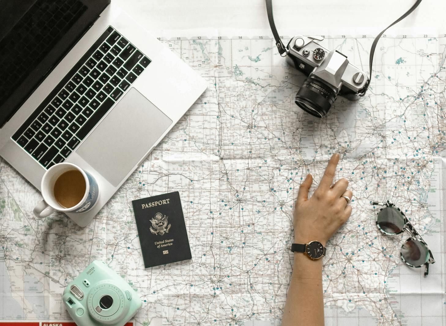A modern workspace setup with a laptop, coffee cup, camera, and various travel accessories neatly arranged on a desk.
