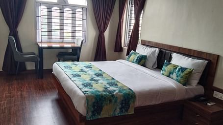 A double bed with chairs & study table next to it inside Premium room with balcony - Ecotel Kolkata