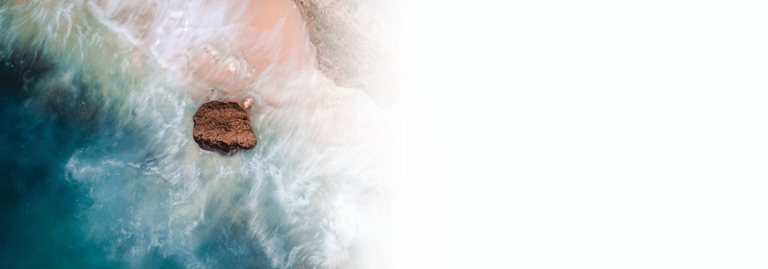 An aerial view of a coastal beach scene with waves crashing around a solitary large rock