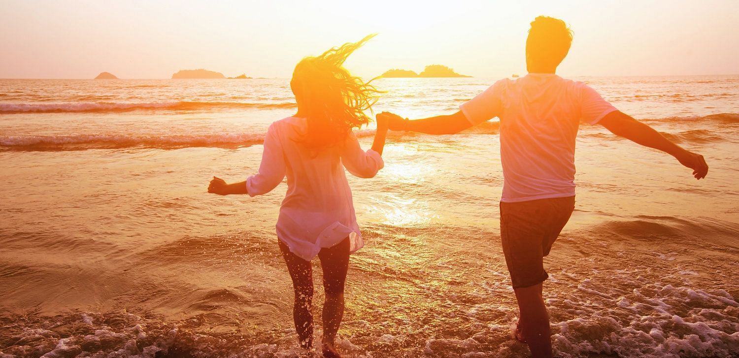 A couple walking hand in hand into the water at the beach during a susnset - Brewery Gulch Inn & Spa