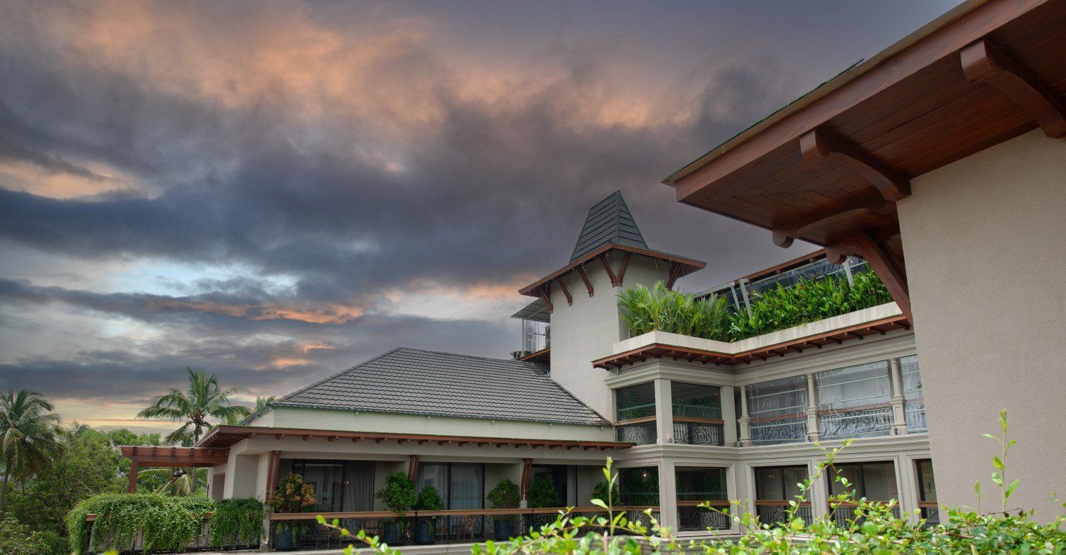 The exterior of The Evren, Vagator, showing the elegant facade, balconies, and the lush green surroundings against a dramatic sky.