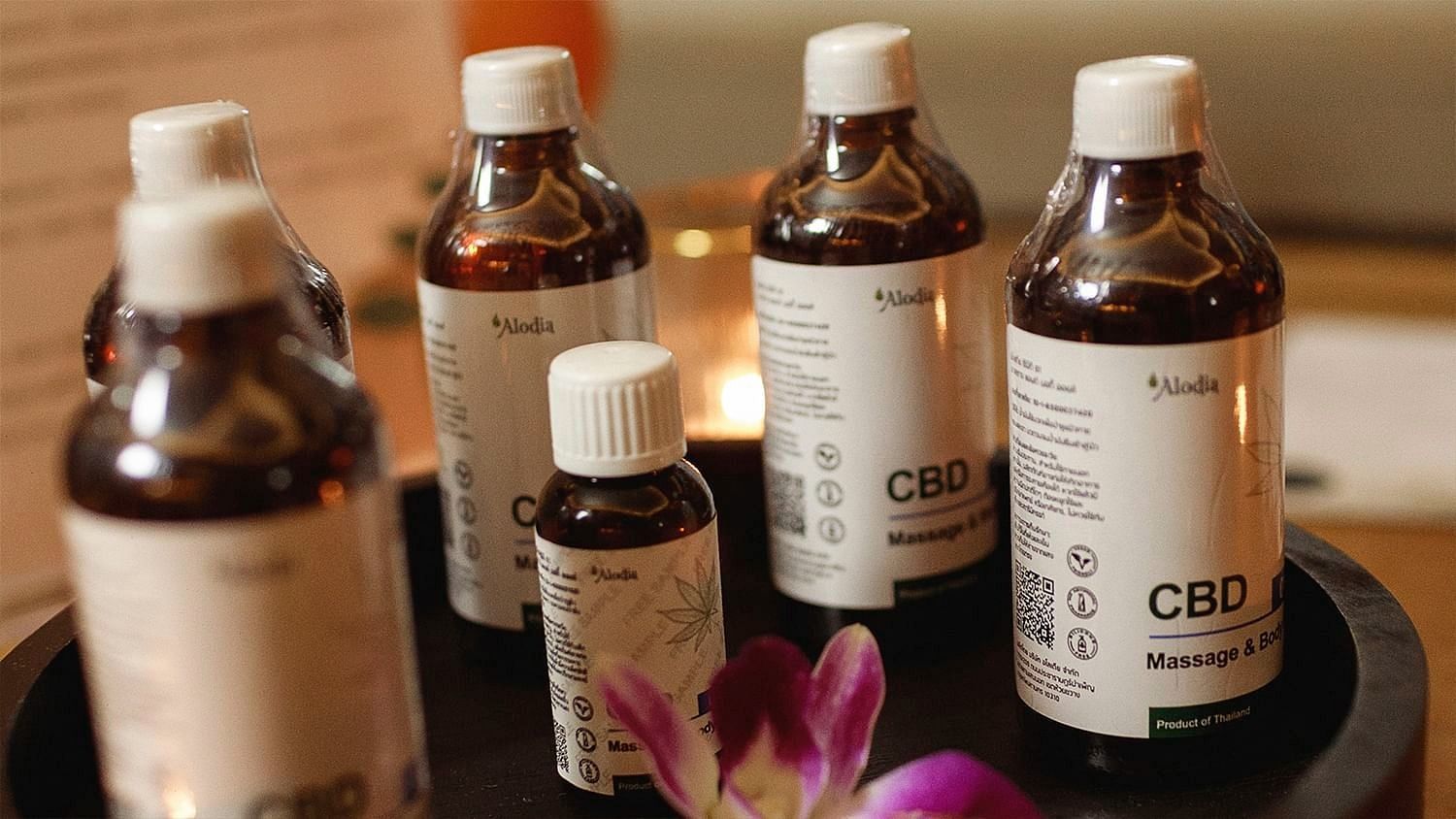 Multiple brown CBD oil bottles with white labels displayed on a black tray with a flower - Maikhao Dream Villa Resort & Spa, Phuket