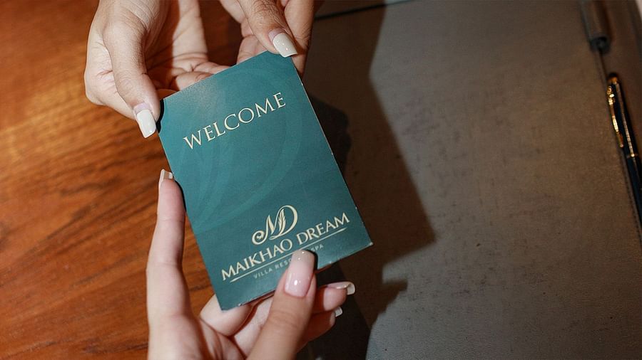 Close-up of hands exchanging a green welcome card with resort branding - Maikhao Dream Villa Resort & Spa, Phuket