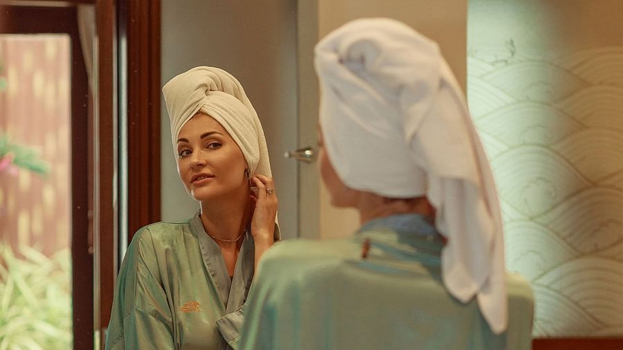 Woman with a towel on her head adjusting her earring in the mirror - Maikhao Dream Villa Resort & Spa, Phuket