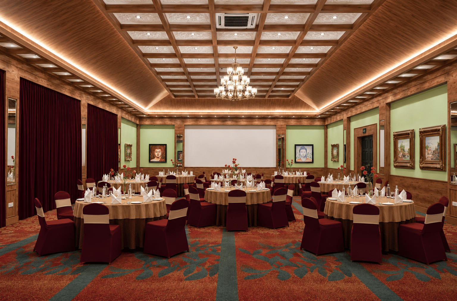 Everest Hall set for a banquet with round tables, maroon chair covers, a projector screen and a chandelier at MAYFAIR Himalayan Spa Resort, Kalimpong.