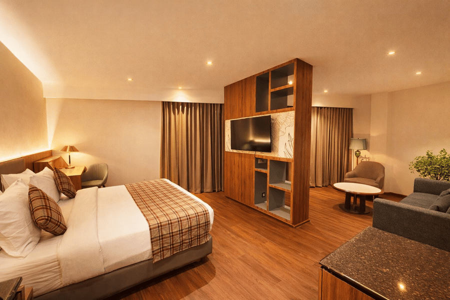 Bedroom at Pride Premier Darjeeling featuring a bed, a work station with chair an desk, a flat TV screen on the wall, and a seating area with sofa set.