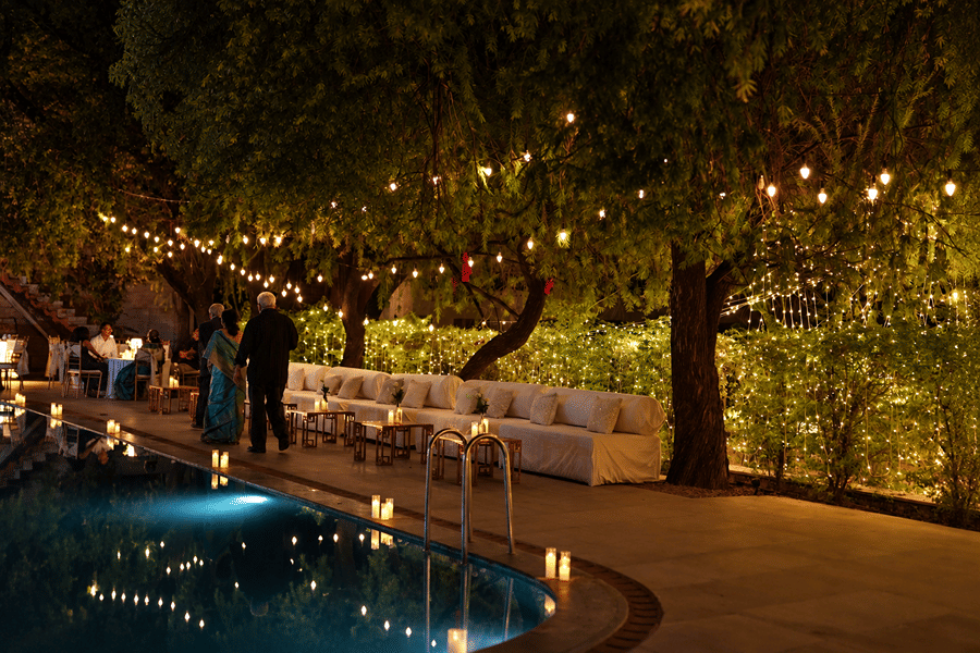 Outdoor swimming pool deck illuminated with hanging fairy lights and lounge seating at night at Umaid Palace.