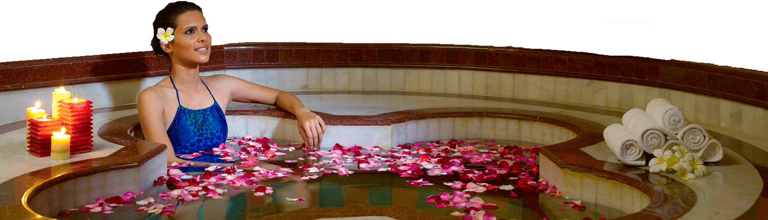 A woman relaxing in a flower-filled bathtub with rose petals and candles on the side.