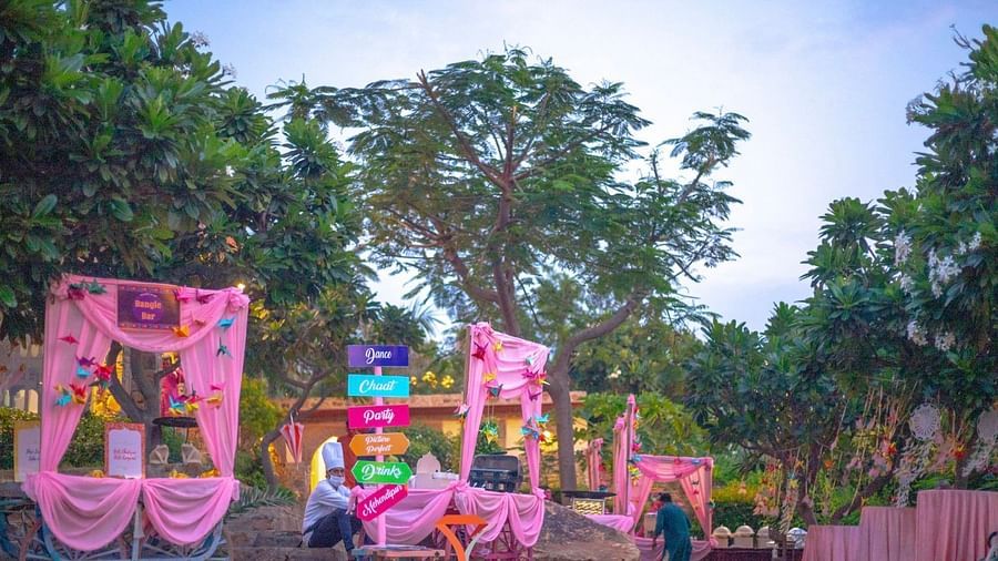 Pink decorations and colorful signs mark an outdoor event space at Tijara Fort-Palace - 19th Century, Alwar, amidst lush greenery.