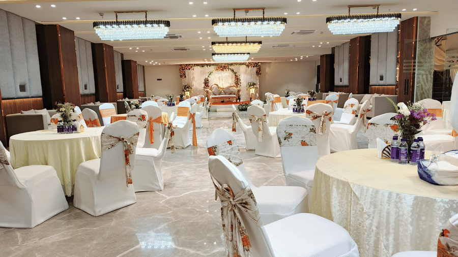 A banquet hall at Hotel 91 HUDA Premier, Gurugram with round tables, chairs, a stage, and decorated setup for gathering.