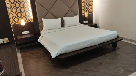 Front view of a room at Hotel Mumbai House with a king bed, patterned headboard, dark wooden flooring, and warm ambient lighting.