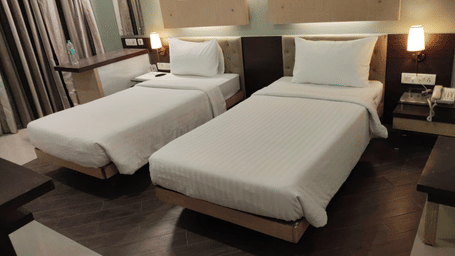 Wide view of a room at Hotel Mumbai House with three single beds, dark wooden flooring, wall sconces, and warm ambient lighting.