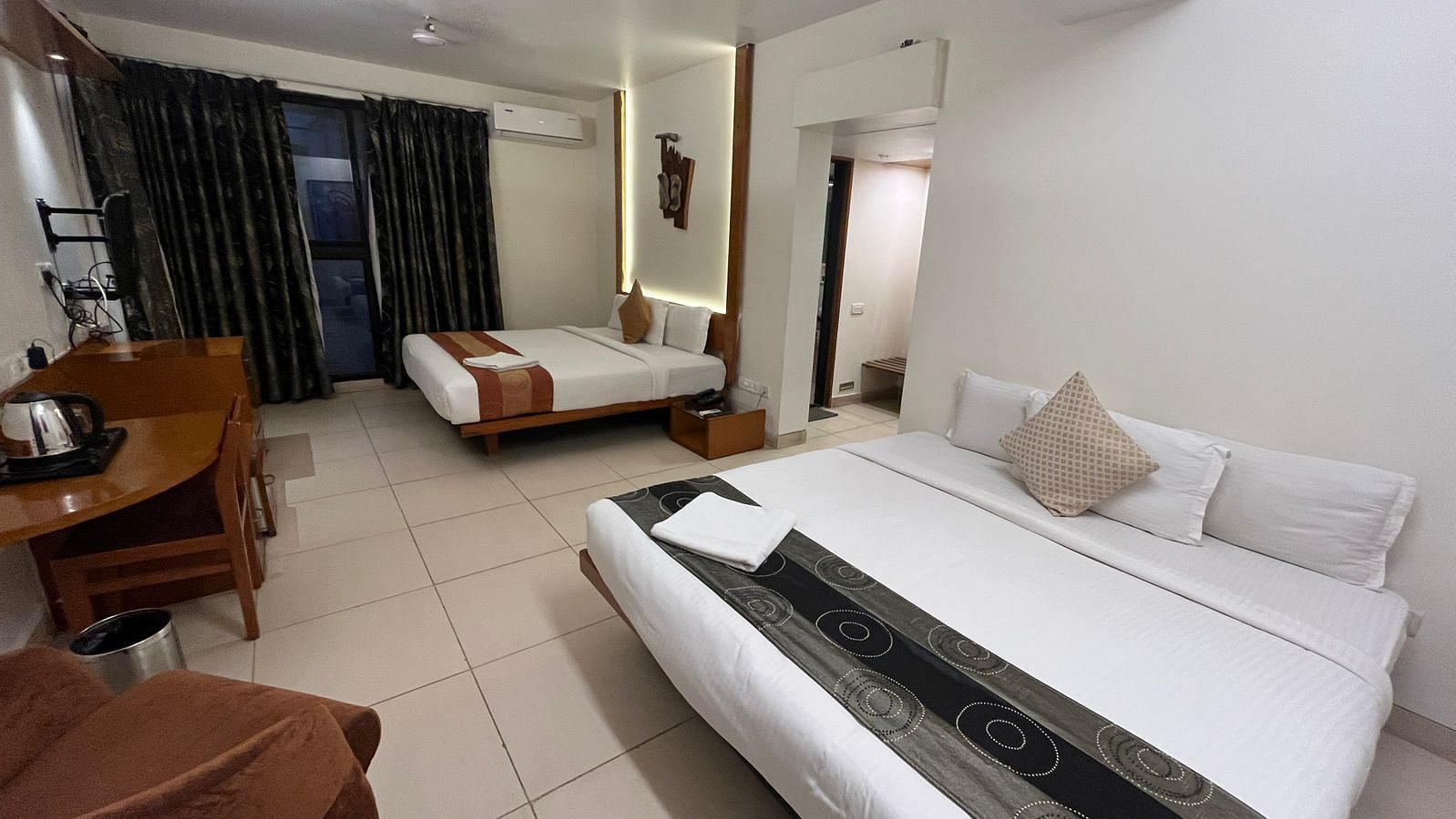 Interior view of a hotel room featuring two beds with white linens and decorative runners, a wooden desk with a kettle, and dark patterned curtains - Astra Hotels & Suites, Spice Garden Layout