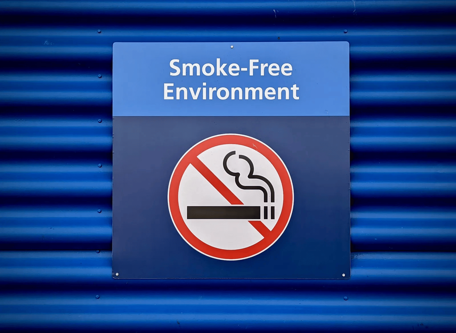 A sign featuring a no-smoking symbol and the text 'Smoke-Free Environment' mounted on a blue wall.