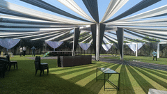 Open lawn venue at Ambrosia Sarovar Portico, Haridwar, with draped canopy, sunlight patterns on grass, and event setup in progress for a daytime function.
