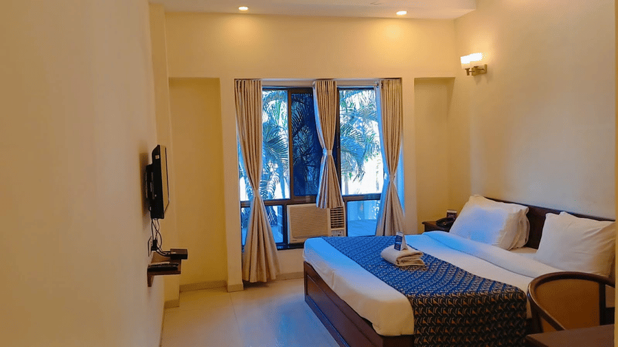 Executive Room at VITS Select, Bharuch featuring a bed, a flat TV screen, an AC, a window with parted curtains providing a view of garden, and a chair with desk.