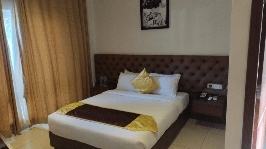 Double bed with padded headboard and bedside table in the Standard Room at Cholaa Dynasty, Kumbakonam.