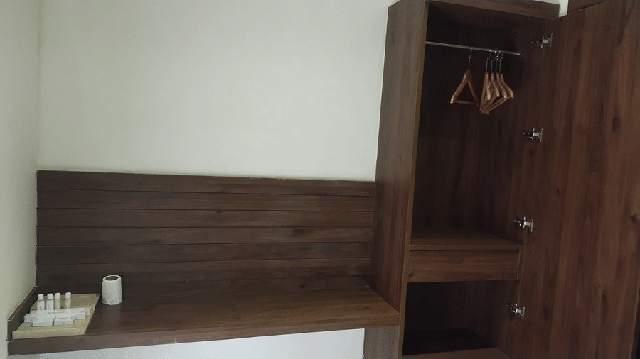 Wooden wardrobe and headboard setup inside the Standard Room at Cholaa Dynasty, Kumbakonam with hanging space and storage shelves.