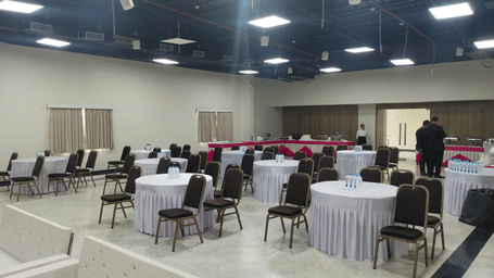 A well-lit event room with clustered style of seating, and a buffet station with staffs standing nearby in Lords Inn Jamnagar