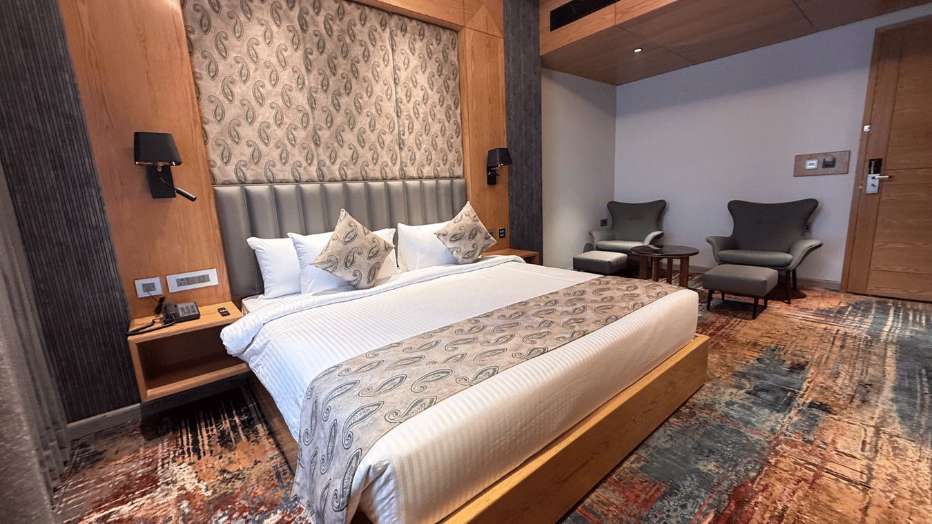 A modern bedroom featuring a king-sized bed with a patterned headboard and vibrant multicoloured carpeting at Ananta Express, Katra.