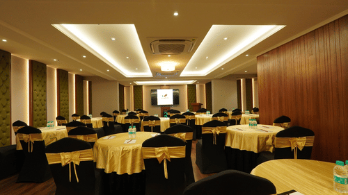Well-lit conference room with a white projection screen, overhead projector, multiple rows of cushioned black chairs, and a grey carpeted floor – Magnus Nexstar Suites, Kalyani Nagar