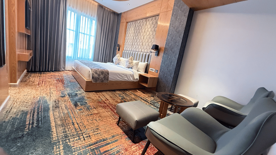 A spacious guest room with a king-sized bed and two grey armchairs placed on a colourful carpet at Ananta Express, Katra.