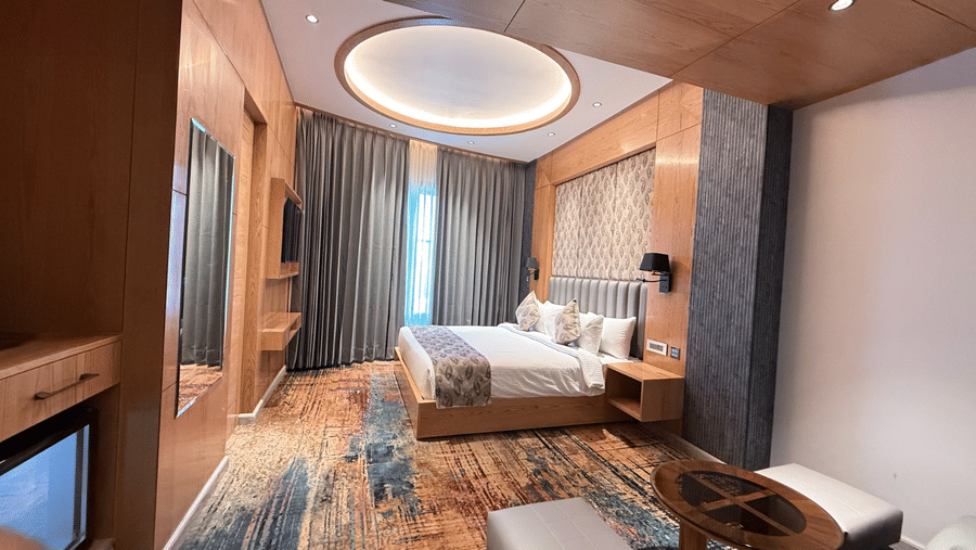 A wide view of a luxury guest room featuring a king-sized bed and large curtains next to a window at Ananta Express, Katra.